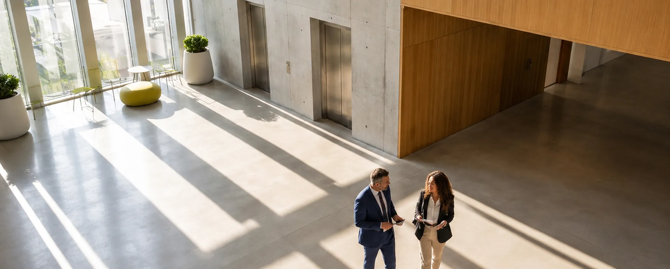 Two colleagues walking and talking in a concrete and wood office lobby